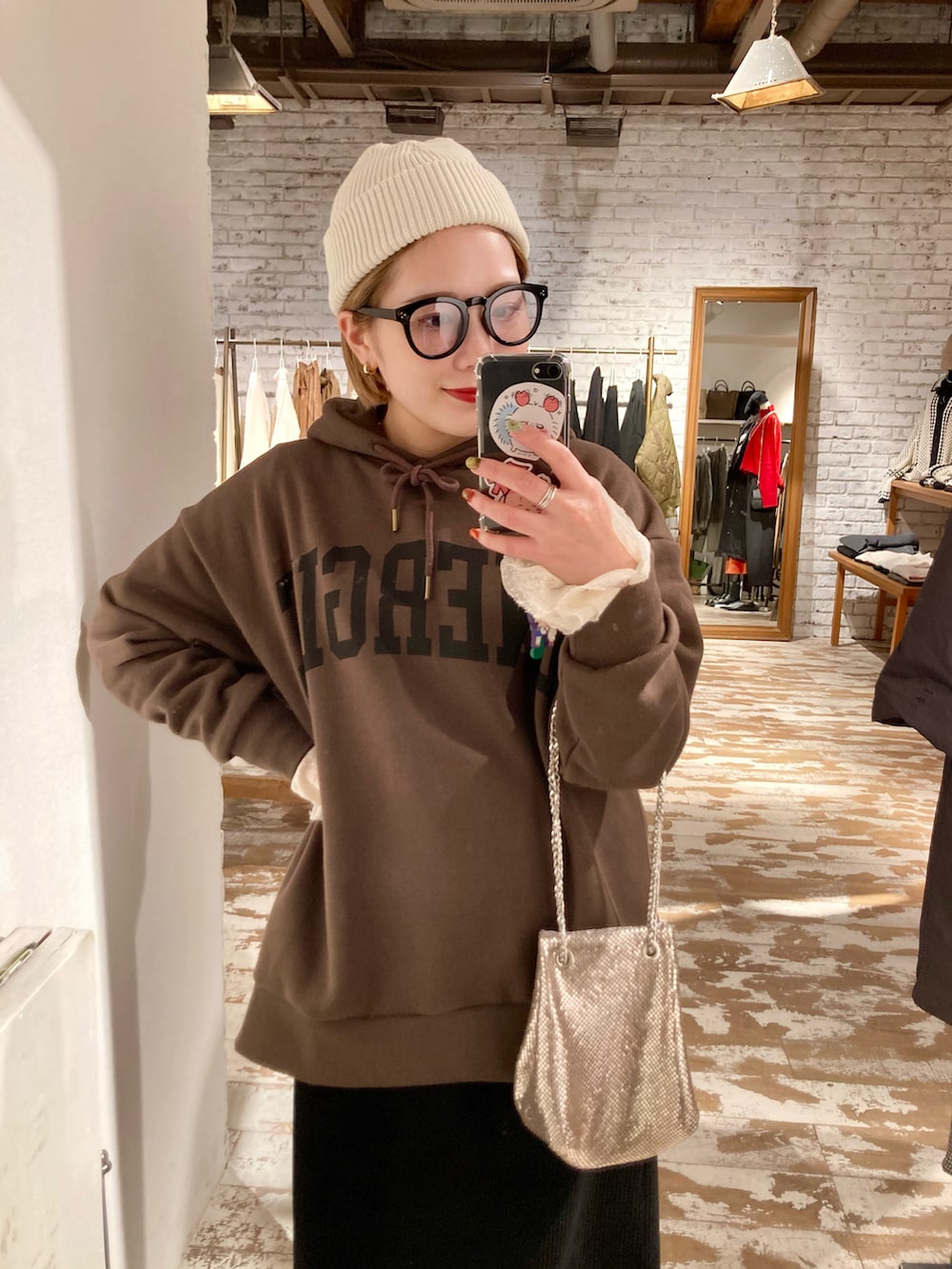 ブラウン系のパーカー、ブラック系のスカート、ゴールド系のショルダーバッグを着用したレディースの秋コーディネートの2枚目の写真