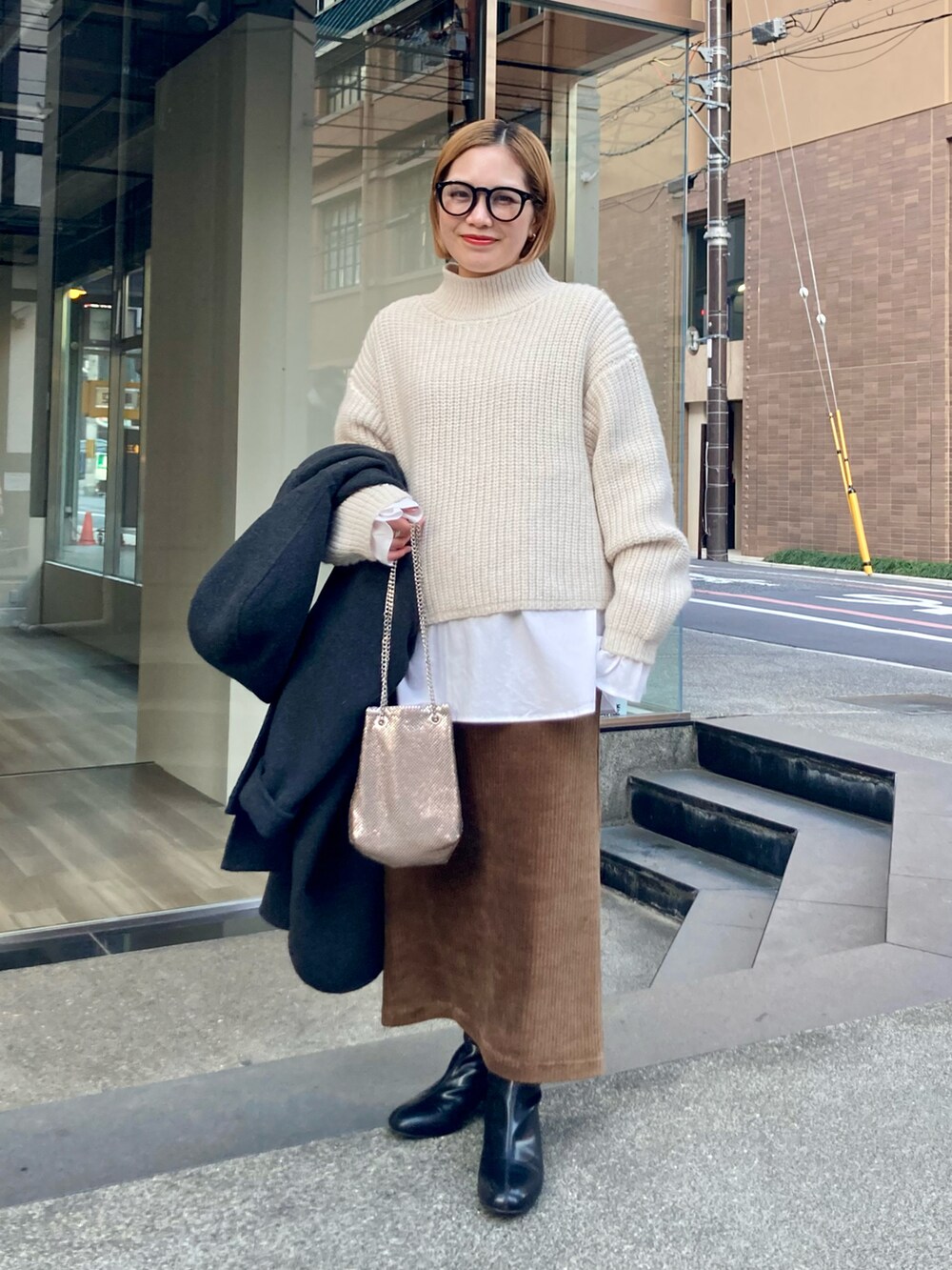 ブラック系のブーツ、ゴールド系のショルダーバッグ、ブラウン系のスカートを着用したレディースの冬コーディネートの3枚目の写真