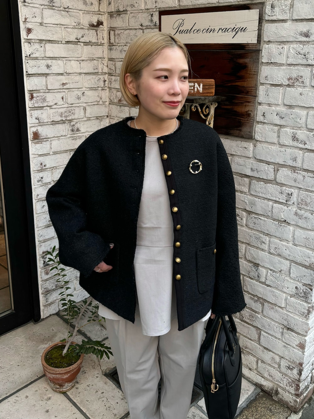 ブラック系のハンドバッグ、ブラック系のノーカラージャケット、ベージュ系のパンツを着用したレディースの冬コーディネートの4枚目の写真