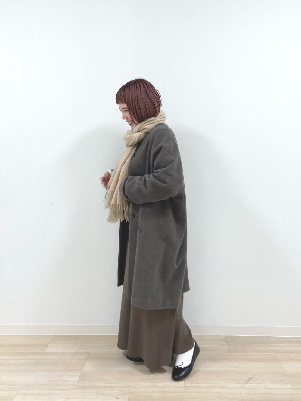 ブラウン系のノーカラーコート、ベージュ系のニット/セーター、ブラウン系のスカートを着用したレディースの冬コーディネートの2枚目の写真