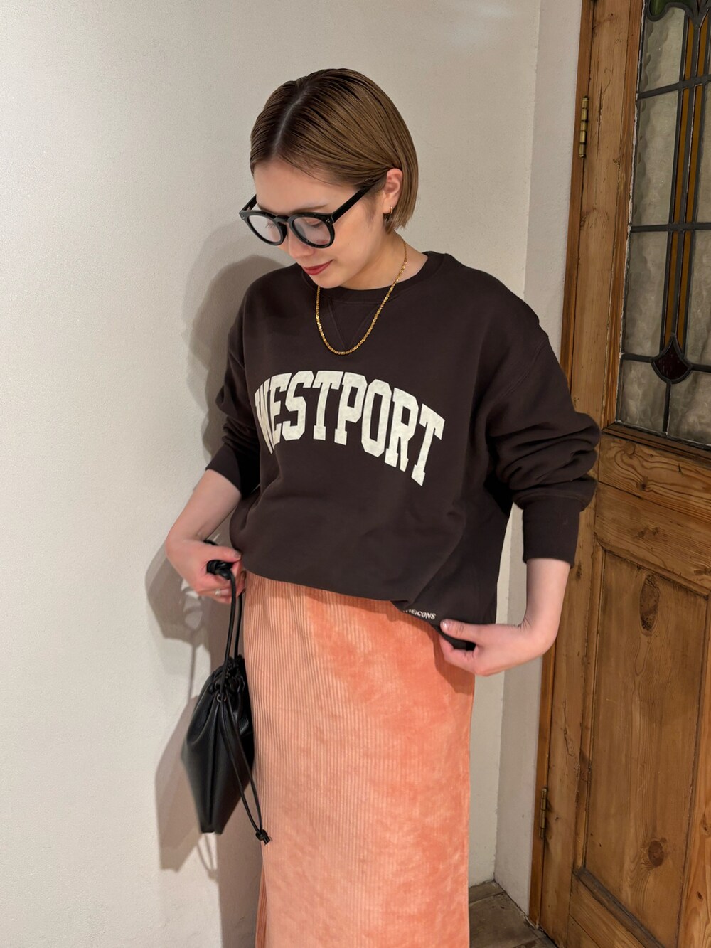 ピンク系のスカート、ブラック系のショルダーバッグ、ブラック系のブーツを着用したレディースの秋コーディネートの2枚目の写真