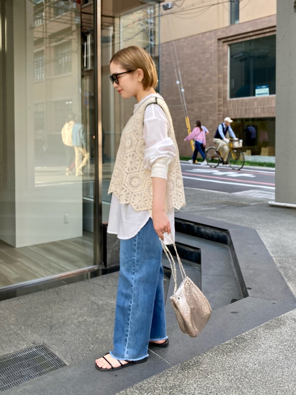 ゴールド系のショルダーバッグ、ブルー系のデニムパンツ、その他のトップスを着用したレディースの春コーディネートの2枚目の写真