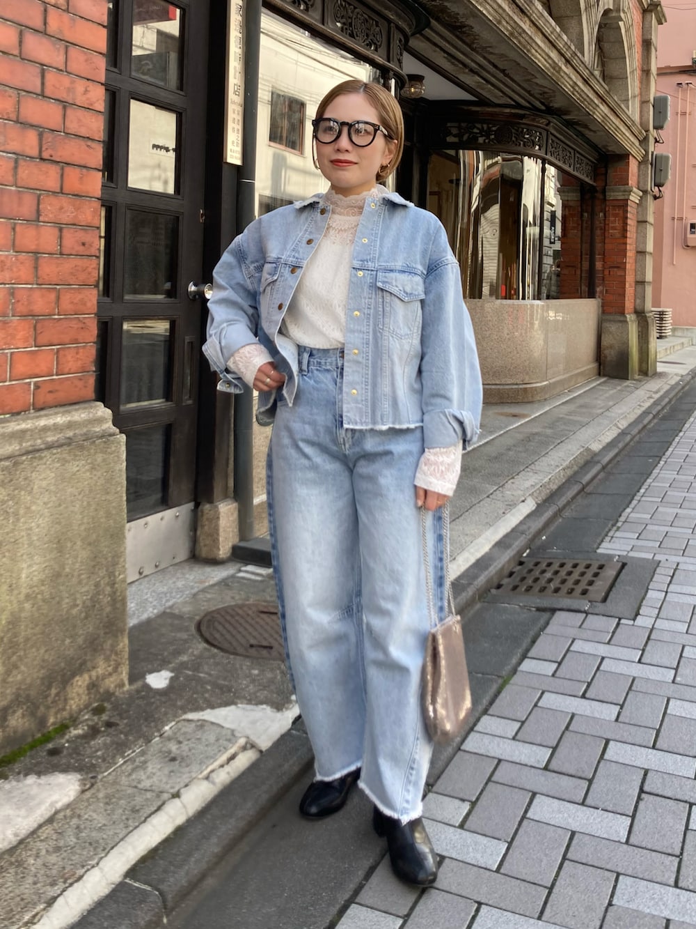 ブラック系のブーツ、ゴールド系のショルダーバッグ、ブルー系のデニムパンツを着用したレディースの冬コーディネートの2枚目の写真