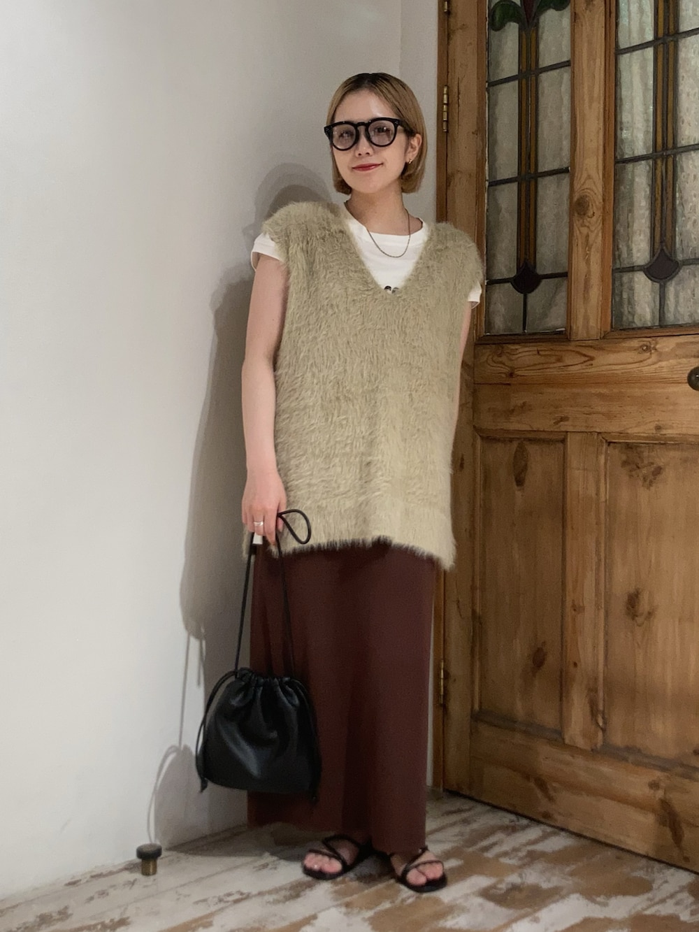 ブラック系のショルダーバッグ、ブラウン系のスカート、ベージュ系のベストを着用したレディースの秋コーディネートの2枚目の写真