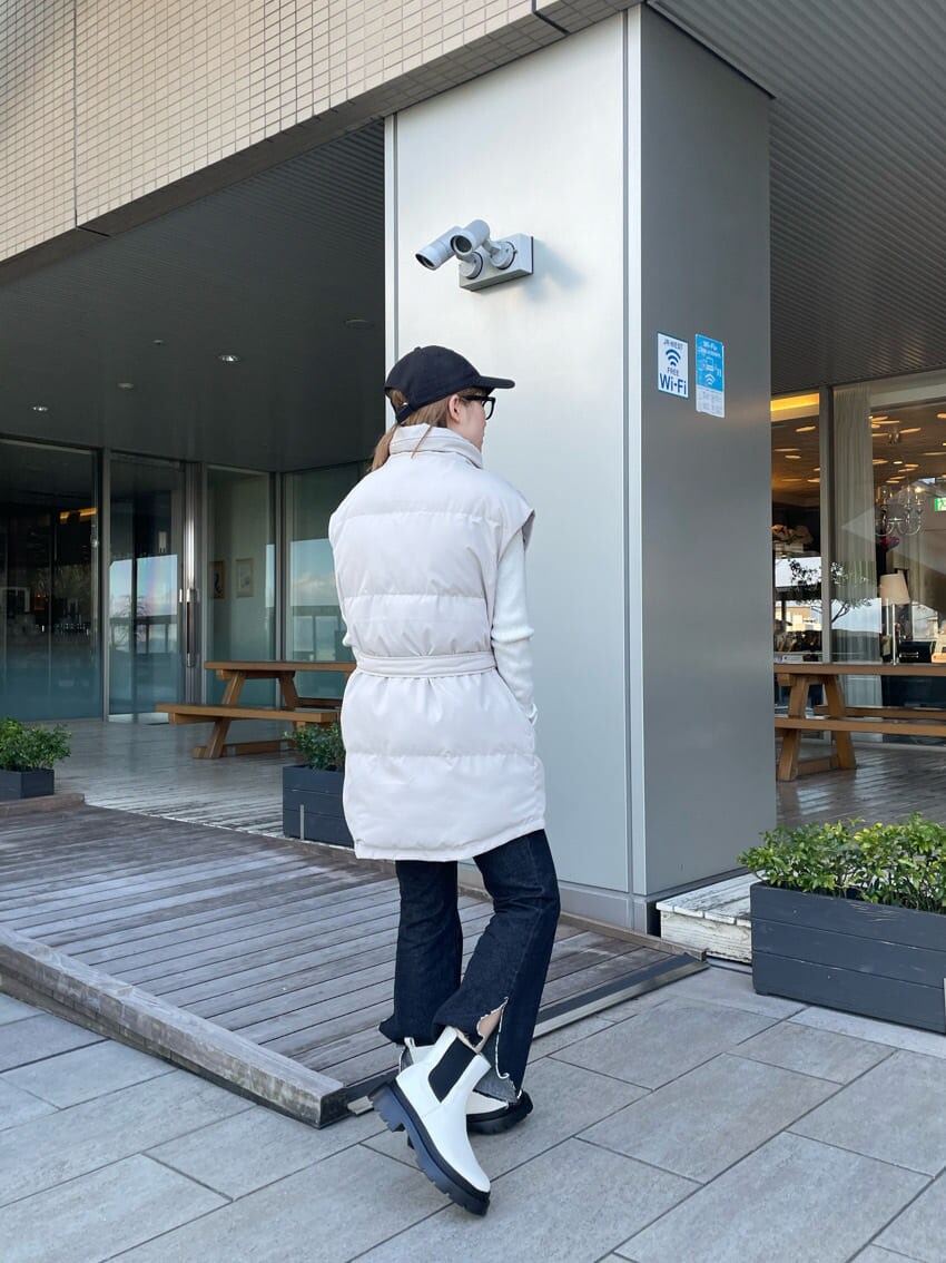 ホワイト系のダウンベスト、ブラック系のデニムパンツ、ホワイト系のニット/セーターを着用したレディースの冬コーディネートの4枚目の写真