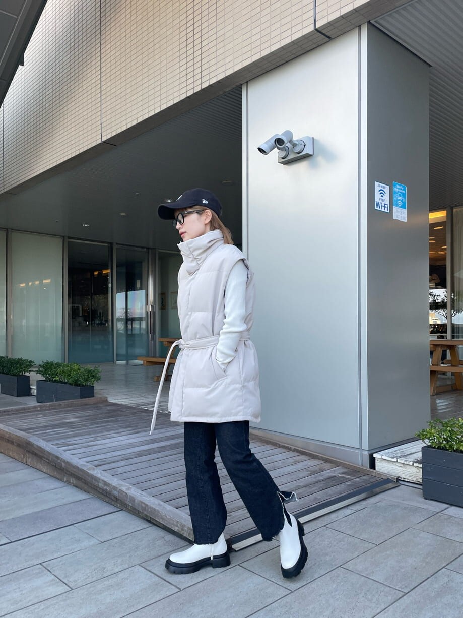 ホワイト系のダウンベスト、ブラック系のデニムパンツ、ホワイト系のニット/セーターを着用したレディースの冬コーディネートの3枚目の写真