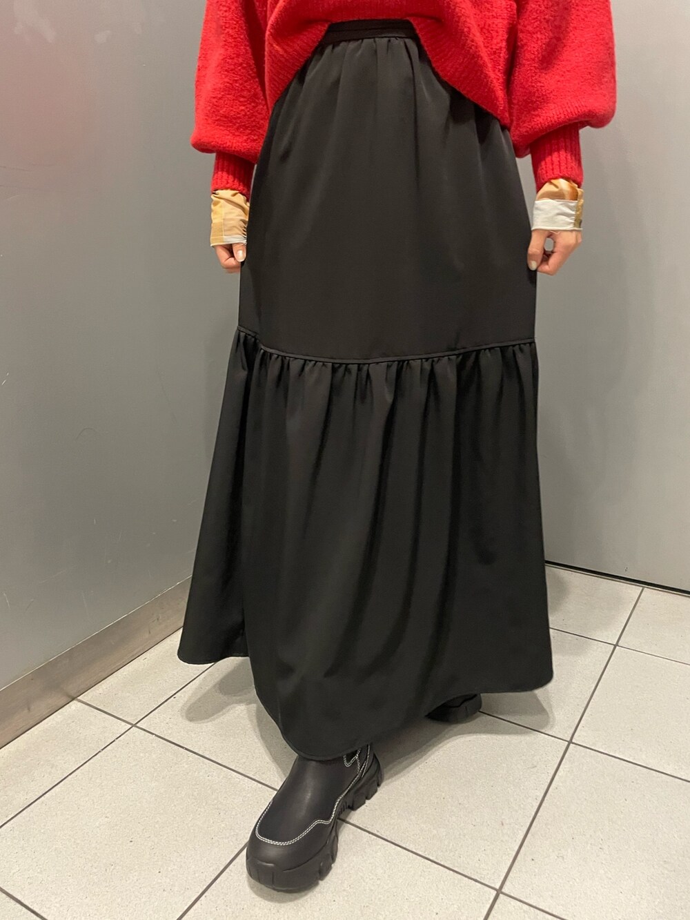 レッド系のニット/セーター、ブラック系のスカート、ブラック系のブーツを着用したレディースの秋コーディネートの7枚目の写真