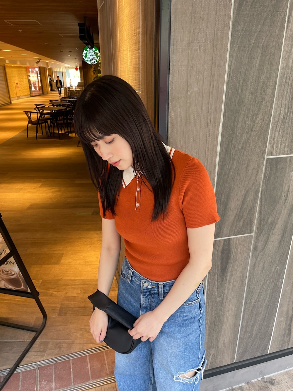 オレンジ系のポロシャツ、ブラック系のハンドバッグを着用したレディースの春コーディネートの4枚目の写真