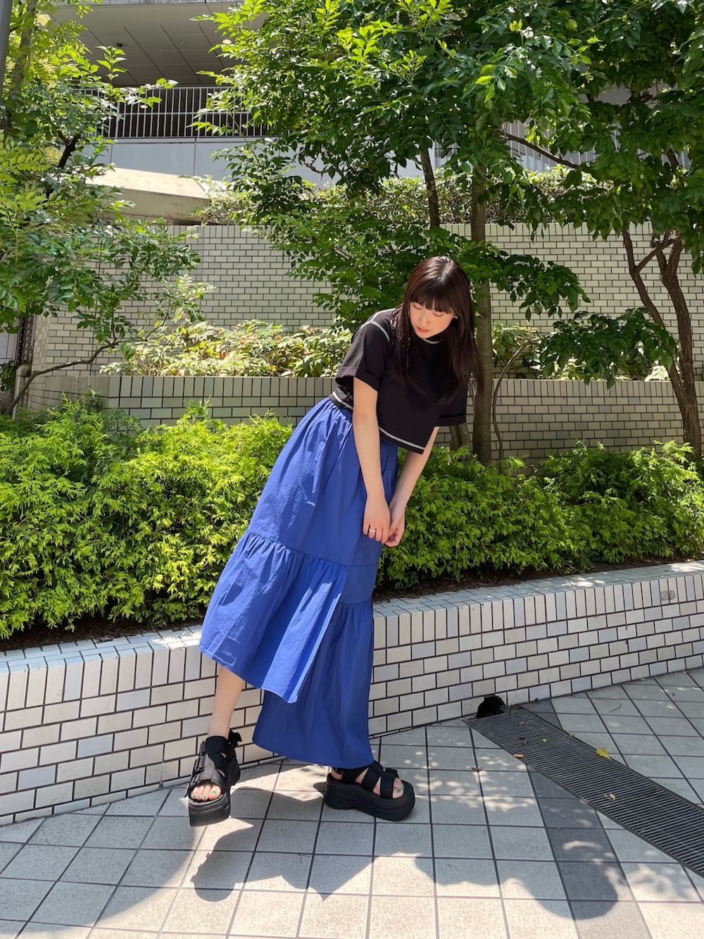 ブラック系のTシャツ/カットソー、ブルー系のスカート、ブラック系のサンダルを着用したレディースの夏コーディネートの2枚目の写真