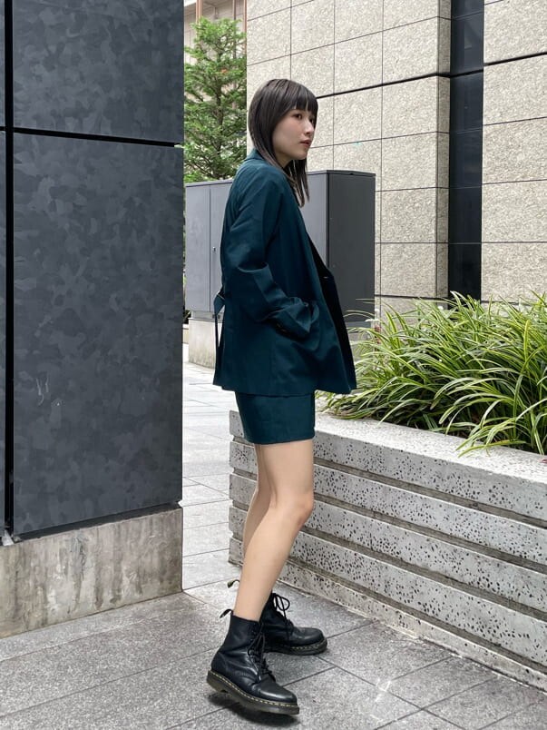 グリーン系のテーラードジャケット、グリーン系のスカート、ブラック系のニット/セーターを着用したレディースの夏コーディネートの2枚目の写真