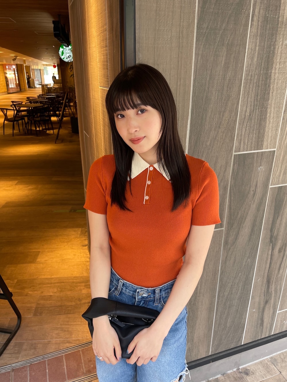 オレンジ系のポロシャツ、ブラック系のハンドバッグを着用したレディースの春コーディネートの3枚目の写真