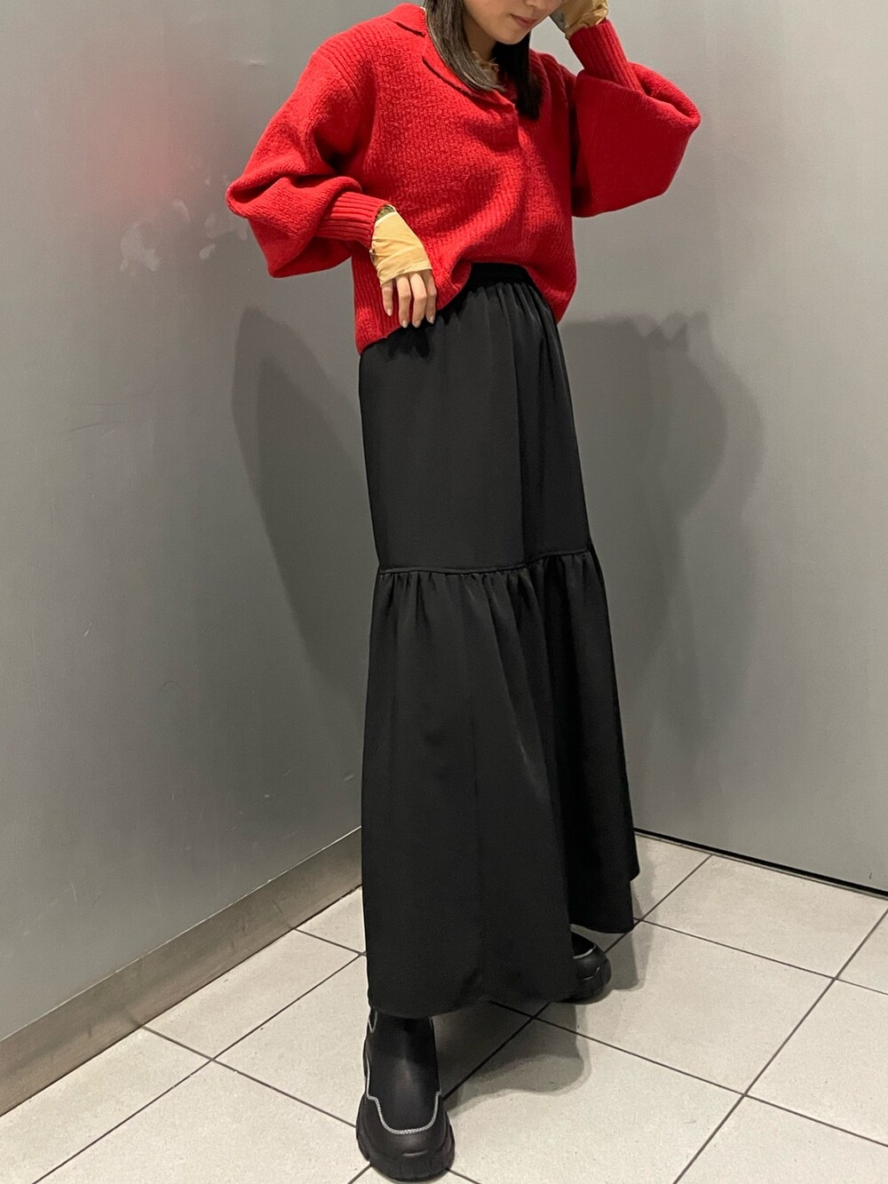レッド系のニット/セーター、ブラック系のスカート、ブラック系のブーツを着用したレディースの秋コーディネートの3枚目の写真