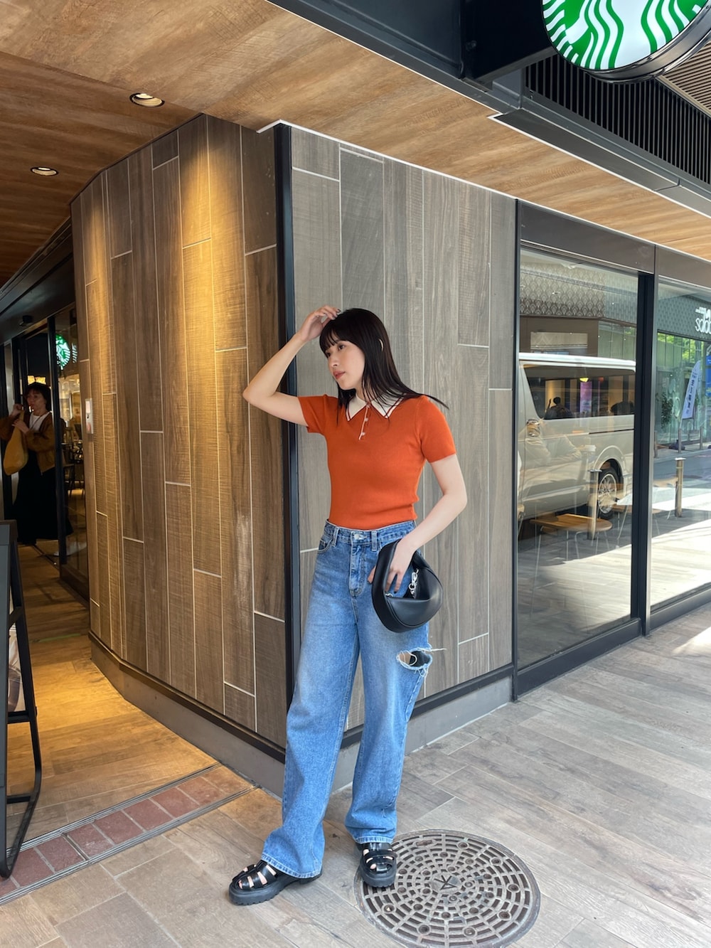 オレンジ系のポロシャツ、ブラック系のハンドバッグを着用したレディースの春コーディネートの2枚目の写真