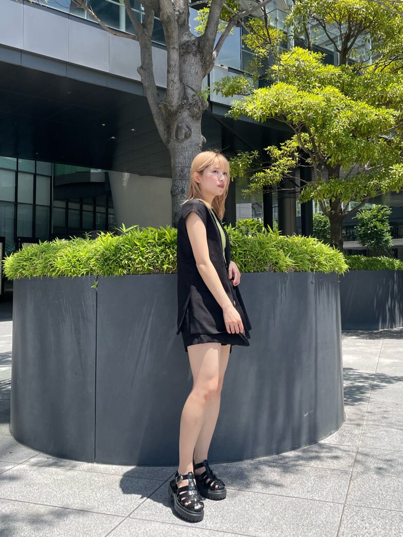 ブラック系のベスト、ブラック系のスラックス、グリーン系のタンクトップを着用したレディースの夏コーディネートの4枚目の写真