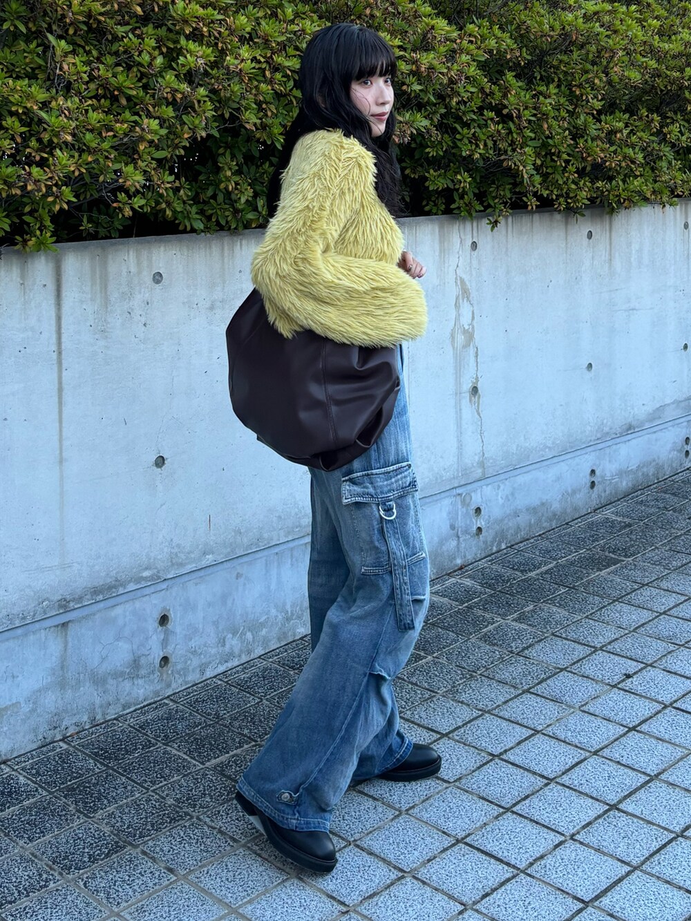 ブルー系のデニムパンツ、ブラウン系のハンドバッグ、イエロー系のニット/セーターを着用したレディースの秋コーディネートの3枚目の写真