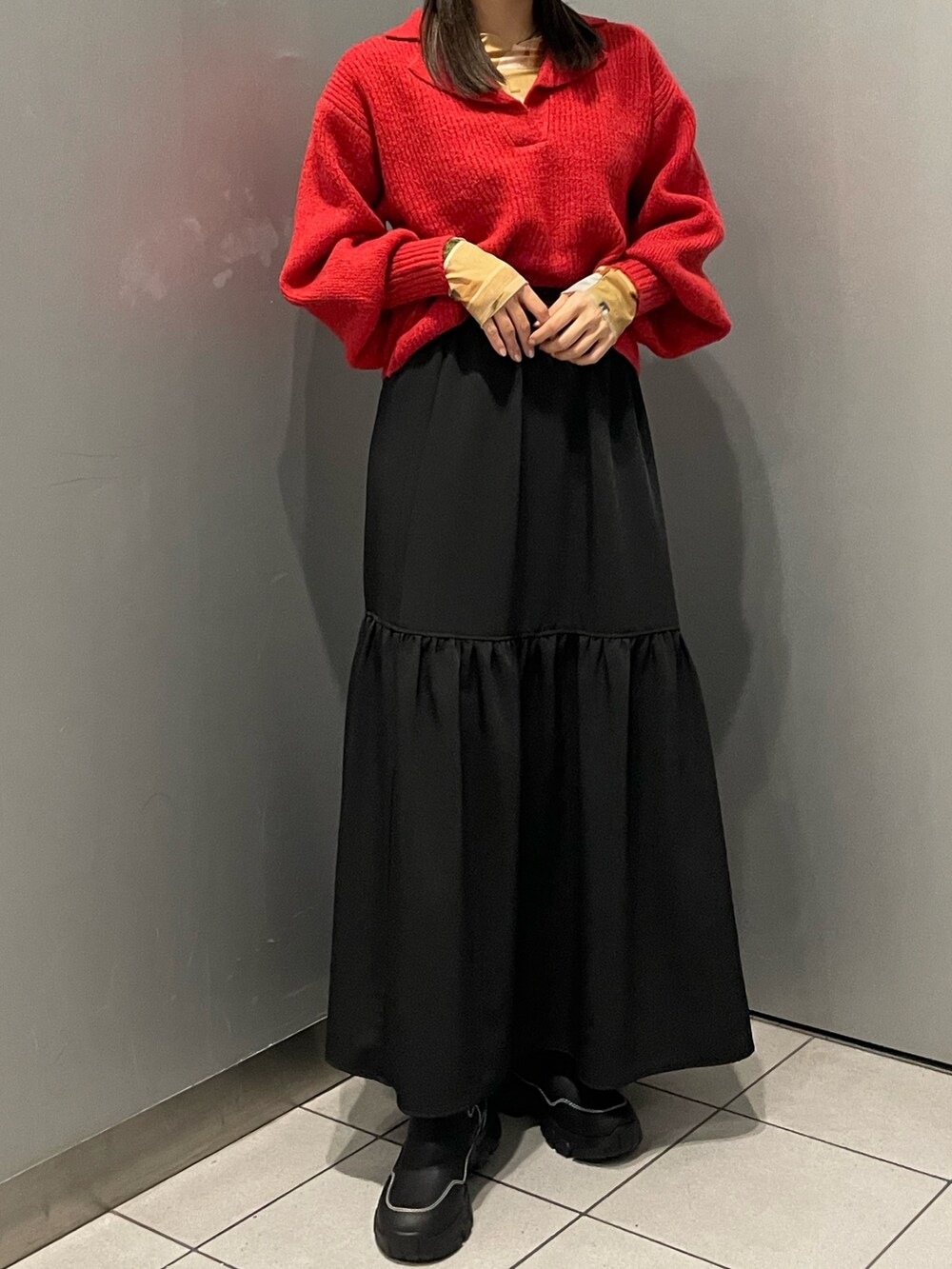 レッド系のニット/セーター、ブラック系のスカート、ブラック系のブーツを着用したレディースの秋コーディネートの4枚目の写真