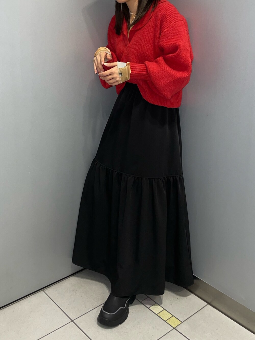 レッド系のニット/セーター、ブラック系のスカート、ブラック系のブーツを着用したレディースの秋コーディネートの2枚目の写真