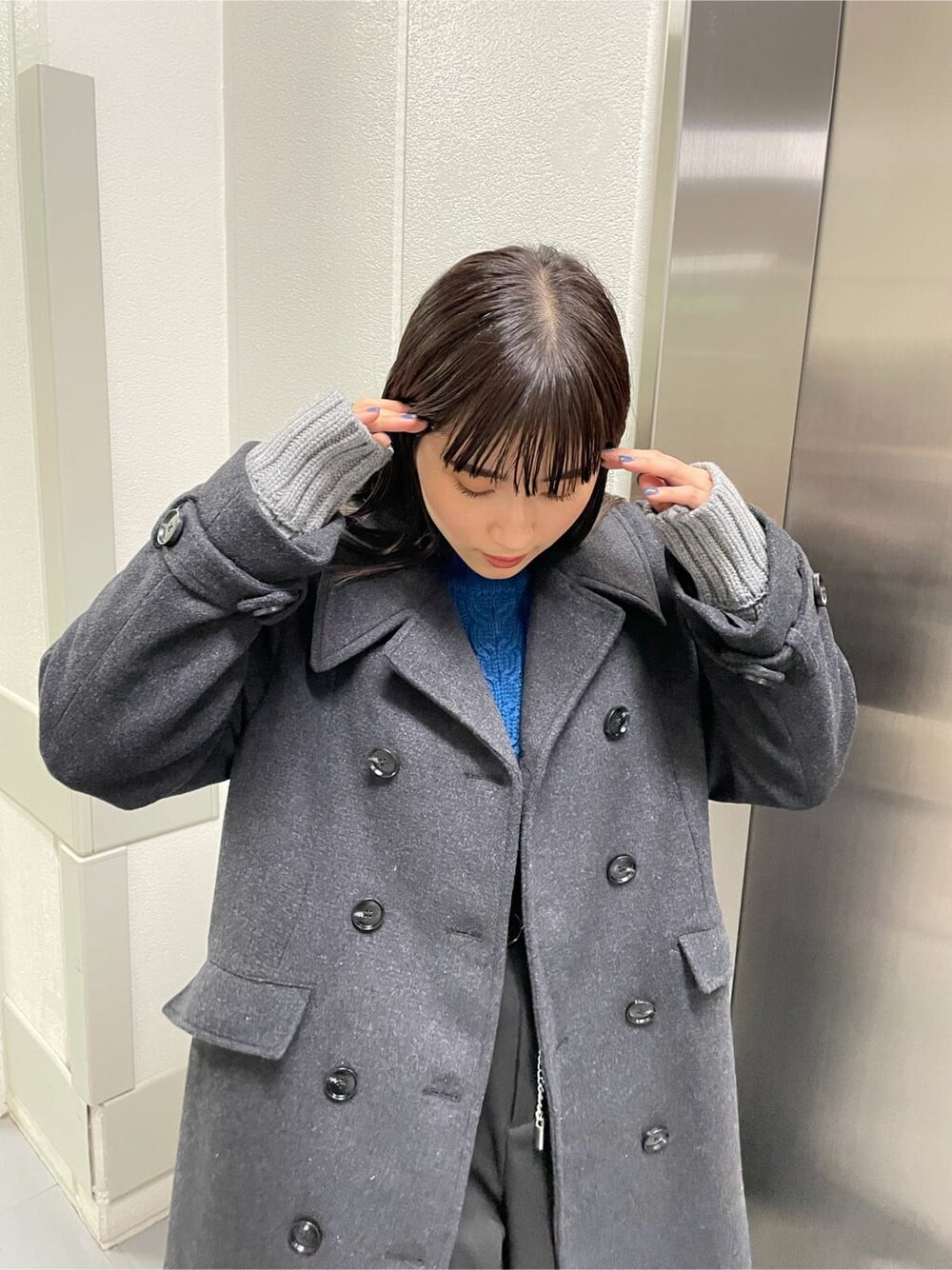 ブルー系のハンドバッグ、ブルー系のニット/セーター、ブラック系のチェスターコートを着用したレディースの秋コーディネートの4枚目の写真