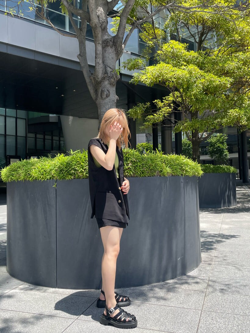 ブラック系のベスト、ブラック系のスラックス、グリーン系のタンクトップを着用したレディースの夏コーディネートの3枚目の写真