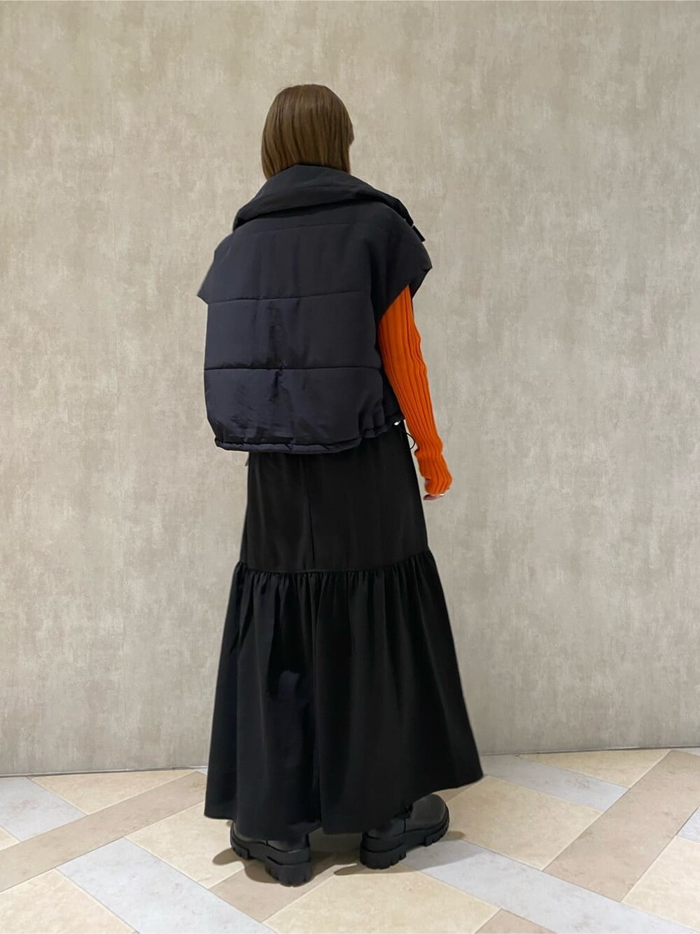 オレンジ系のニット/セーター、ブラック系のダウンベスト、ブラック系のブーツを着用したレディースの秋コーディネートの5枚目の写真