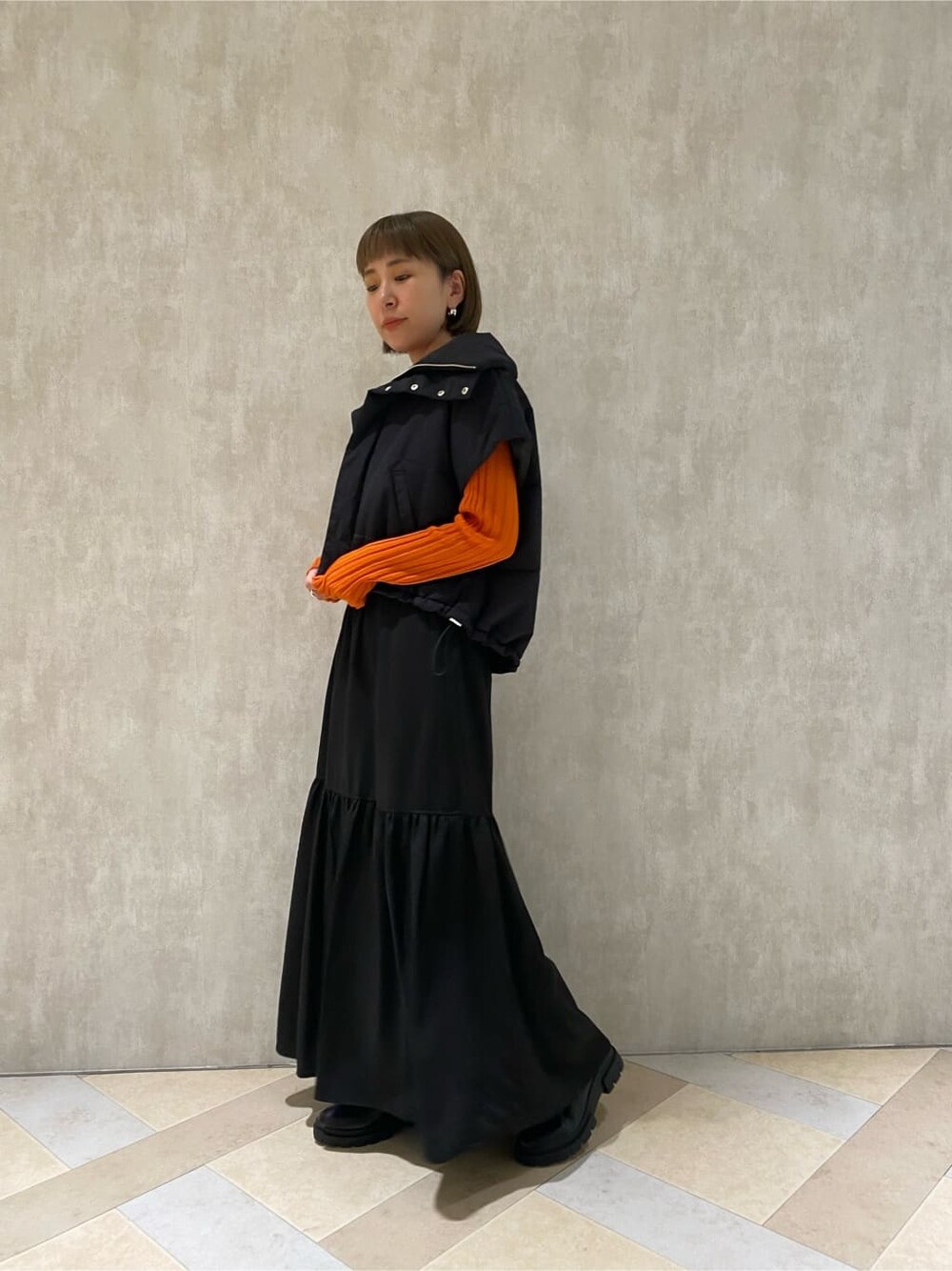 オレンジ系のニット/セーター、ブラック系のダウンベスト、ブラック系のブーツを着用したレディースの秋コーディネートの3枚目の写真