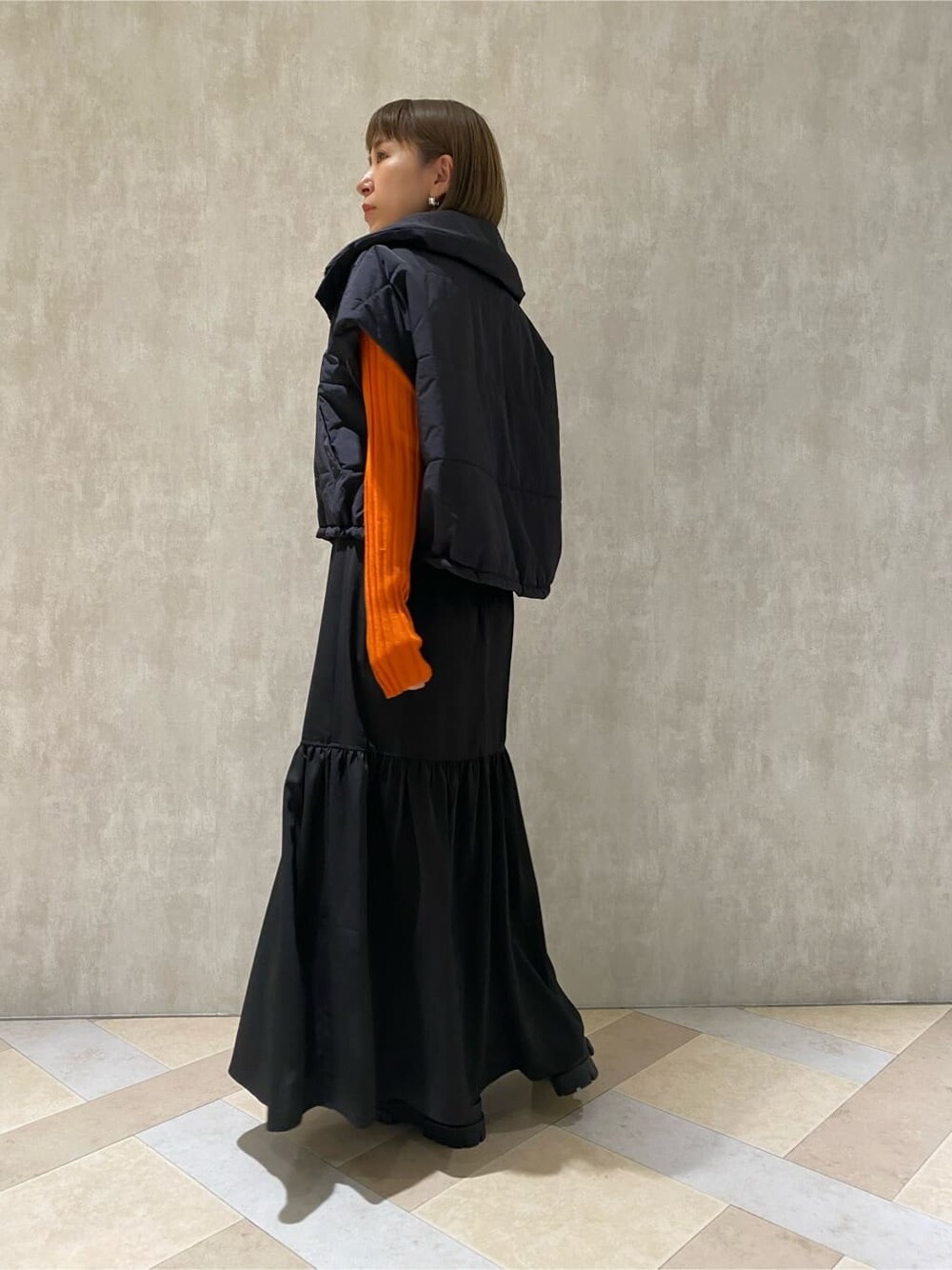 オレンジ系のニット/セーター、ブラック系のダウンベスト、ブラック系のブーツを着用したレディースの秋コーディネートの4枚目の写真