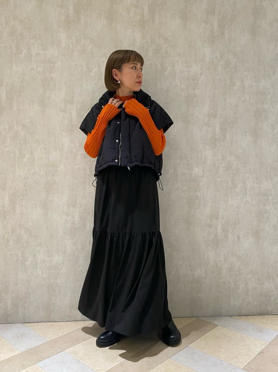 オレンジ系のニット/セーター、ブラック系のダウンベスト、ブラック系のブーツを着用したレディースの秋コーディネートの2枚目の写真