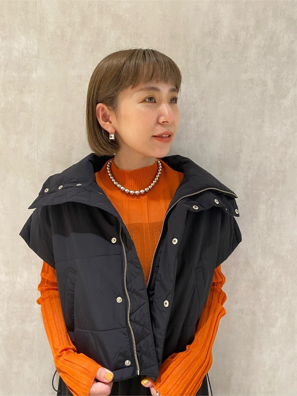 オレンジ系のニット/セーター、ブラック系のダウンベスト、ブラック系のブーツを着用したレディースの秋コーディネートの6枚目の写真