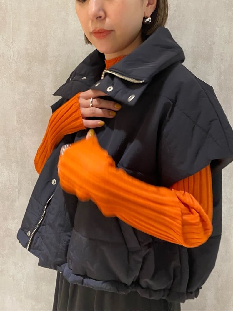 オレンジ系のニット/セーター、ブラック系のダウンベスト、ブラック系のブーツを着用したレディースの秋コーディネートの7枚目の写真