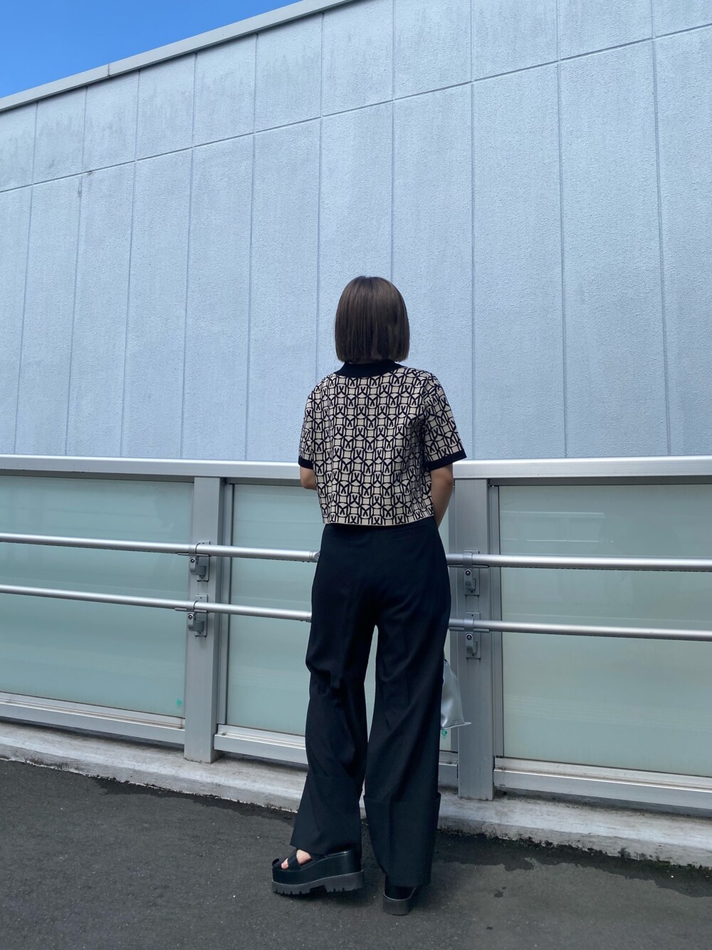 ブラック系のポロシャツ、グレー系のスラックス、ブラック系のサンダルを着用したレディースの春コーディネートの4枚目の写真