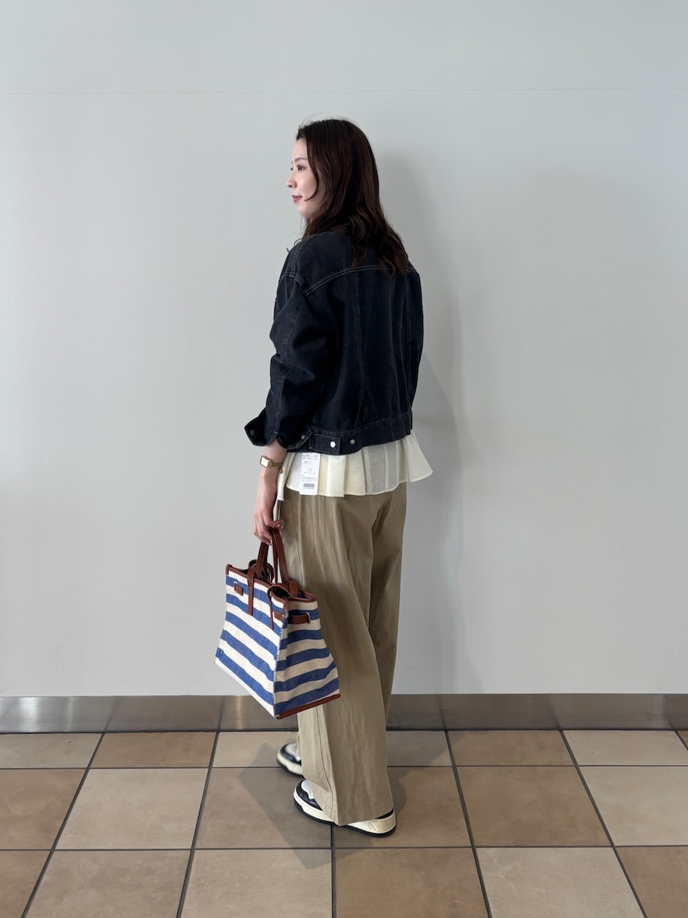 ブラック系のノーカラージャケット、ベージュ系のチノパンツ、ブルー系のショルダーバッグを着用したレディースの春コーディネートの2枚目の写真