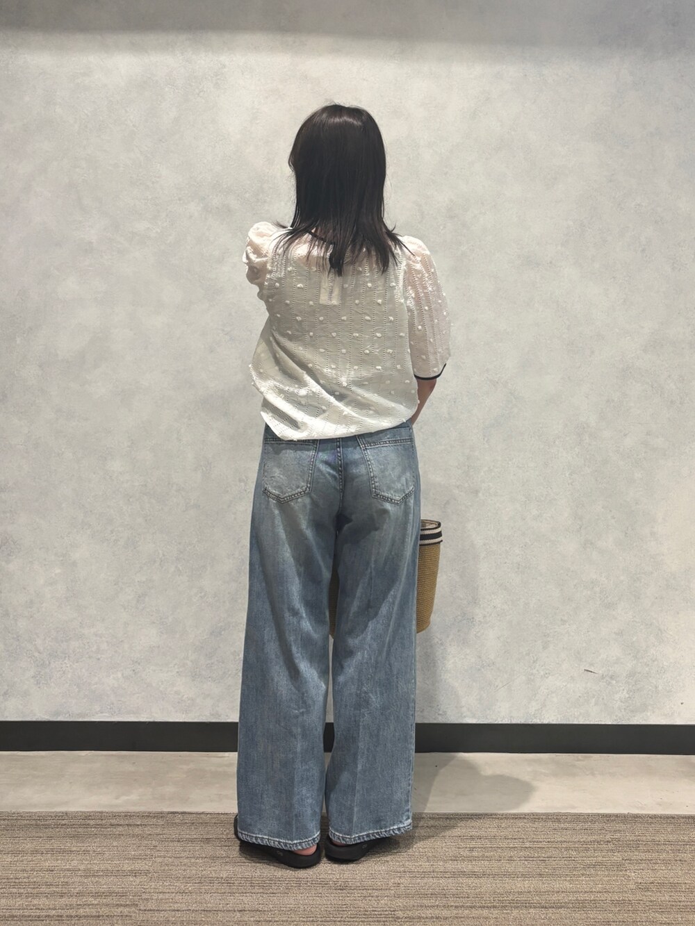 ブルー系のデニムパンツ、ベージュ系のかごバッグ、ホワイト系のシャツ/ブラウスを着用したレディースの夏コーディネートの2枚目の写真