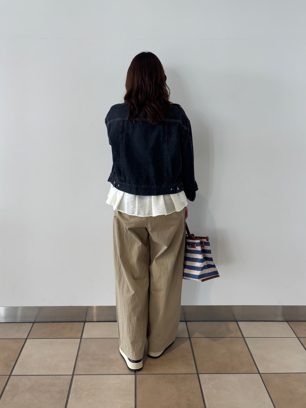 ブラック系のノーカラージャケット、ベージュ系のチノパンツ、ブルー系のショルダーバッグを着用したレディースの春コーディネートの3枚目の写真