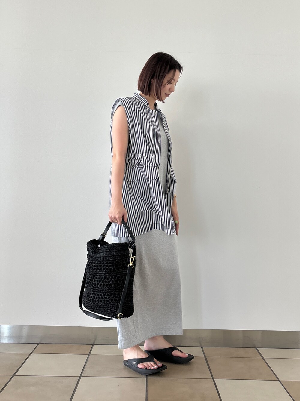 ブルー系のベスト、グレー系のワンピース、ブラック系のかごバッグを着用したレディースの夏コーディネートの2枚目の写真