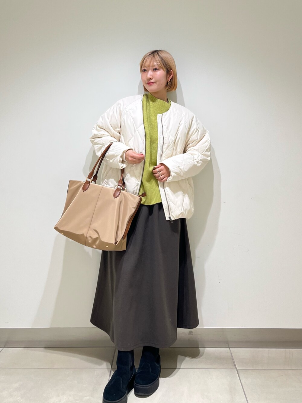 ブラウン系のスカート、ホワイト系のダウンジャケット/コート、グリーン系のニット/セーターを着用したレディースの冬コーディネートの2枚目の写真