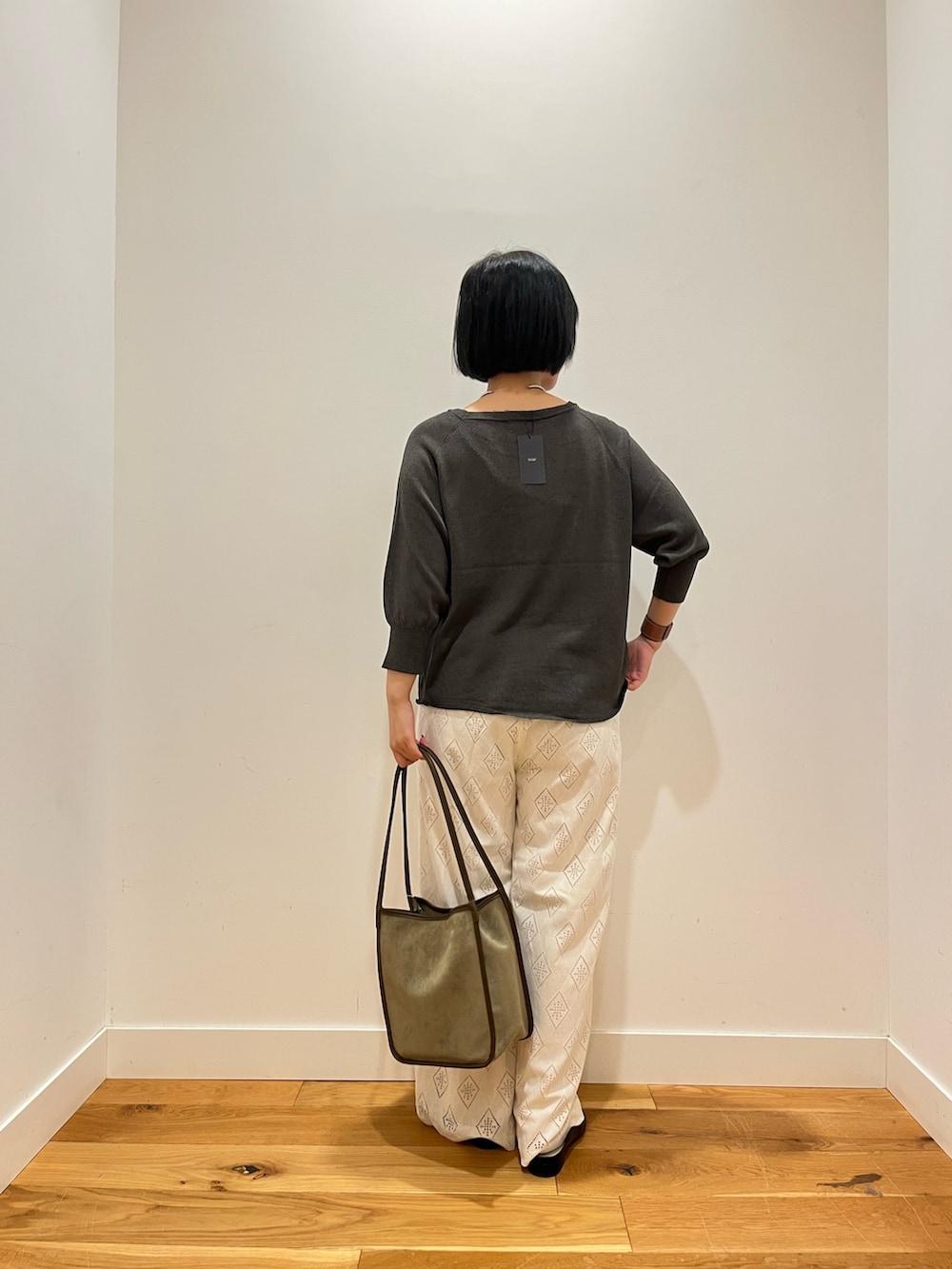 グレー系のニット/セーター、ホワイト系のその他パンツ、グリーン系のトートバッグを着用したレディースの秋コーディネートの3枚目の写真