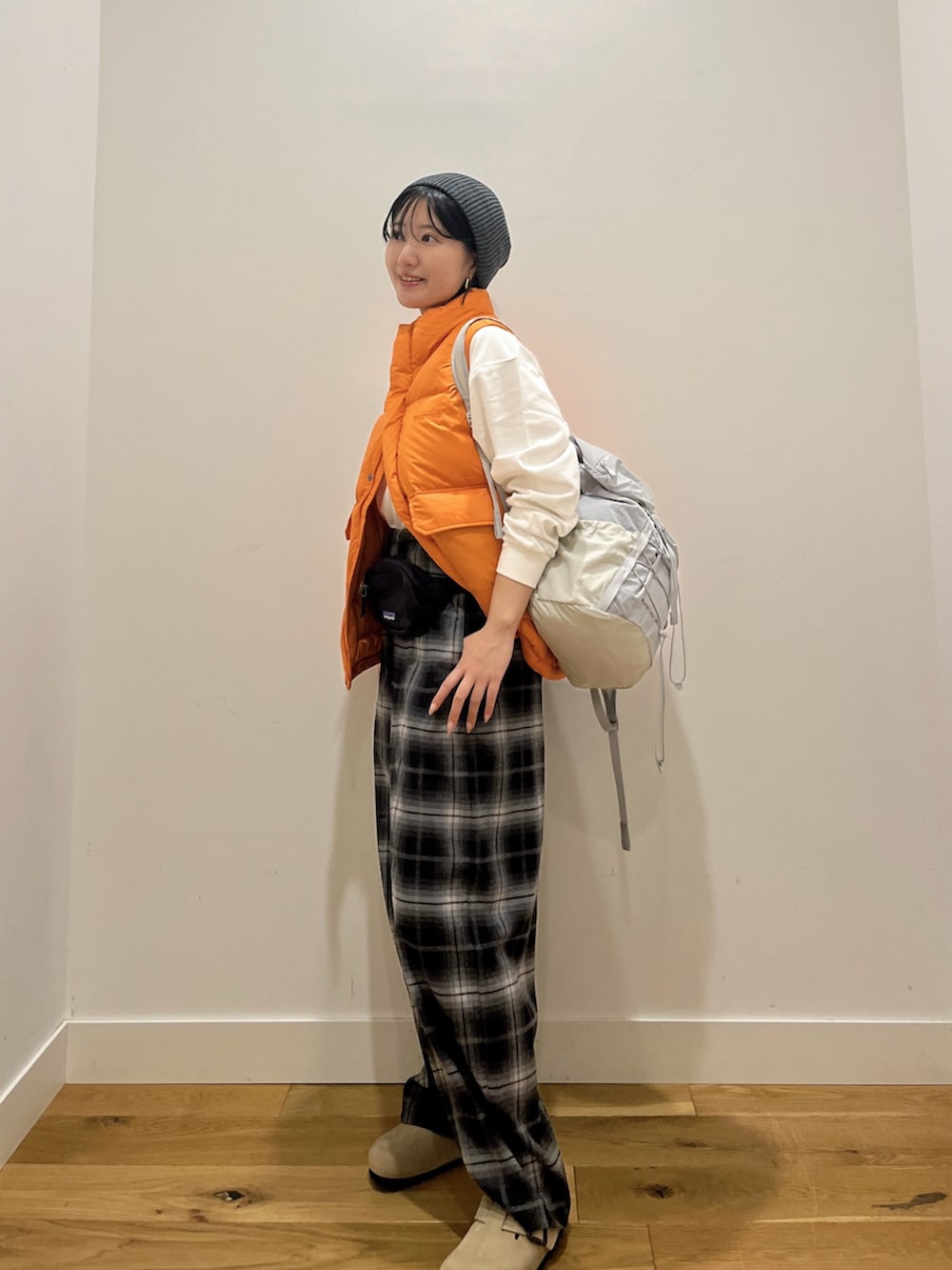 オレンジ系のダウンベスト、ホワイト系のTシャツ/カットソー、グレー系のバックパック/リュックを着用したレディースの秋コーディネートの3枚目の写真