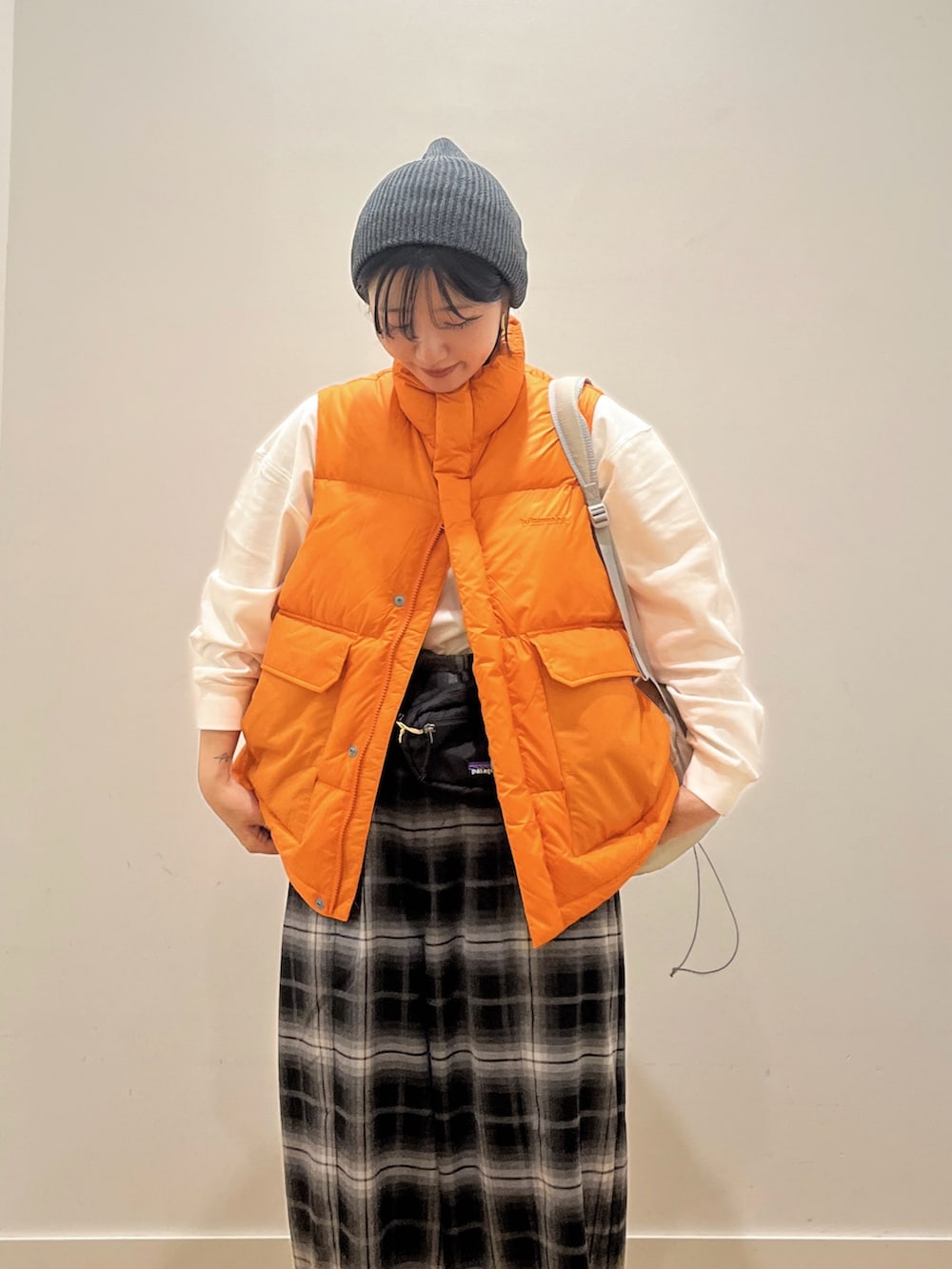 オレンジ系のダウンベスト、ホワイト系のTシャツ/カットソー、グレー系のバックパック/リュックを着用したレディースの秋コーディネートの4枚目の写真