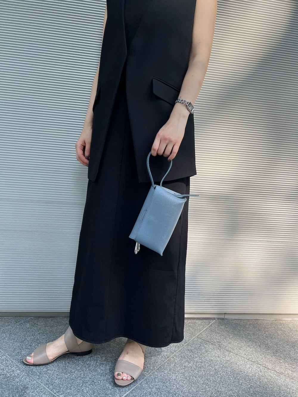 グレー系のハンドバッグ、ブラック系のワンピース、ブラック系のベストを着用したレディースの春コーディネートの2枚目の写真