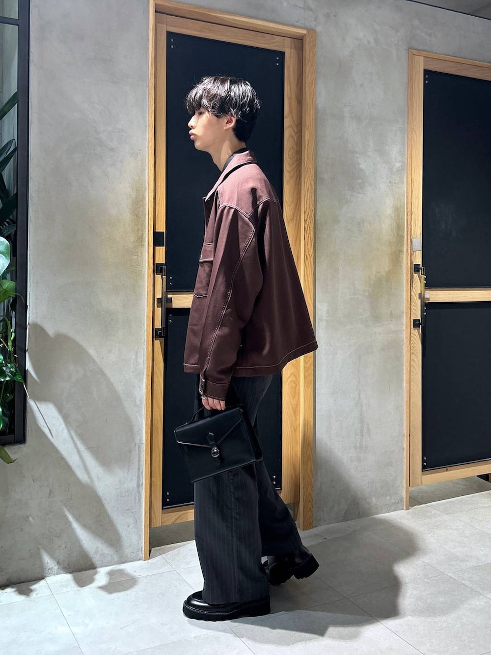 グレー系のスラックス、ブラウン系のブルゾン、ブラック系のショルダーバッグを着用したメンズの秋コーディネートの3枚目の写真