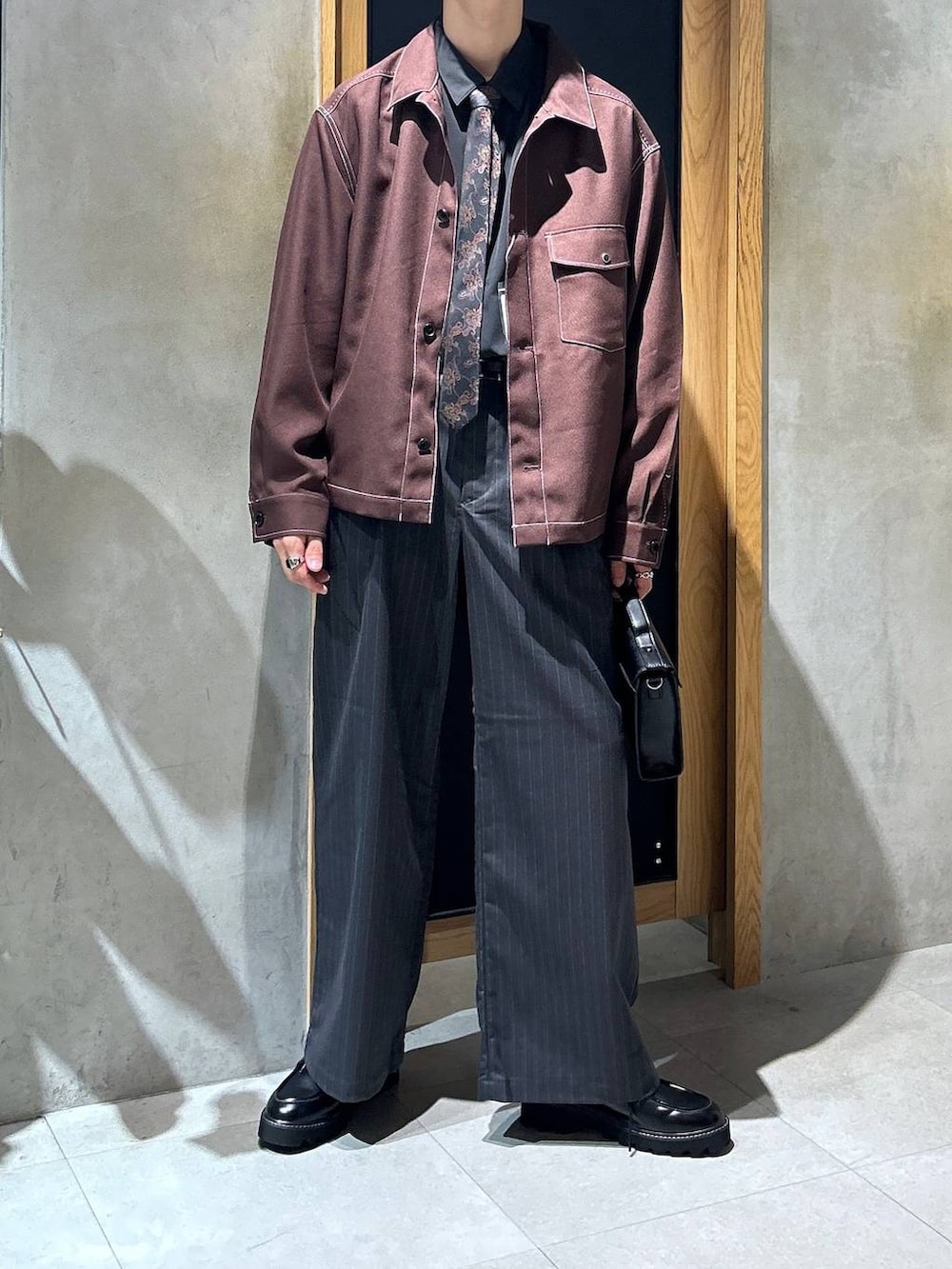 グレー系のスラックス、ブラウン系のブルゾン、ブラック系のショルダーバッグを着用したメンズの秋コーディネートの2枚目の写真