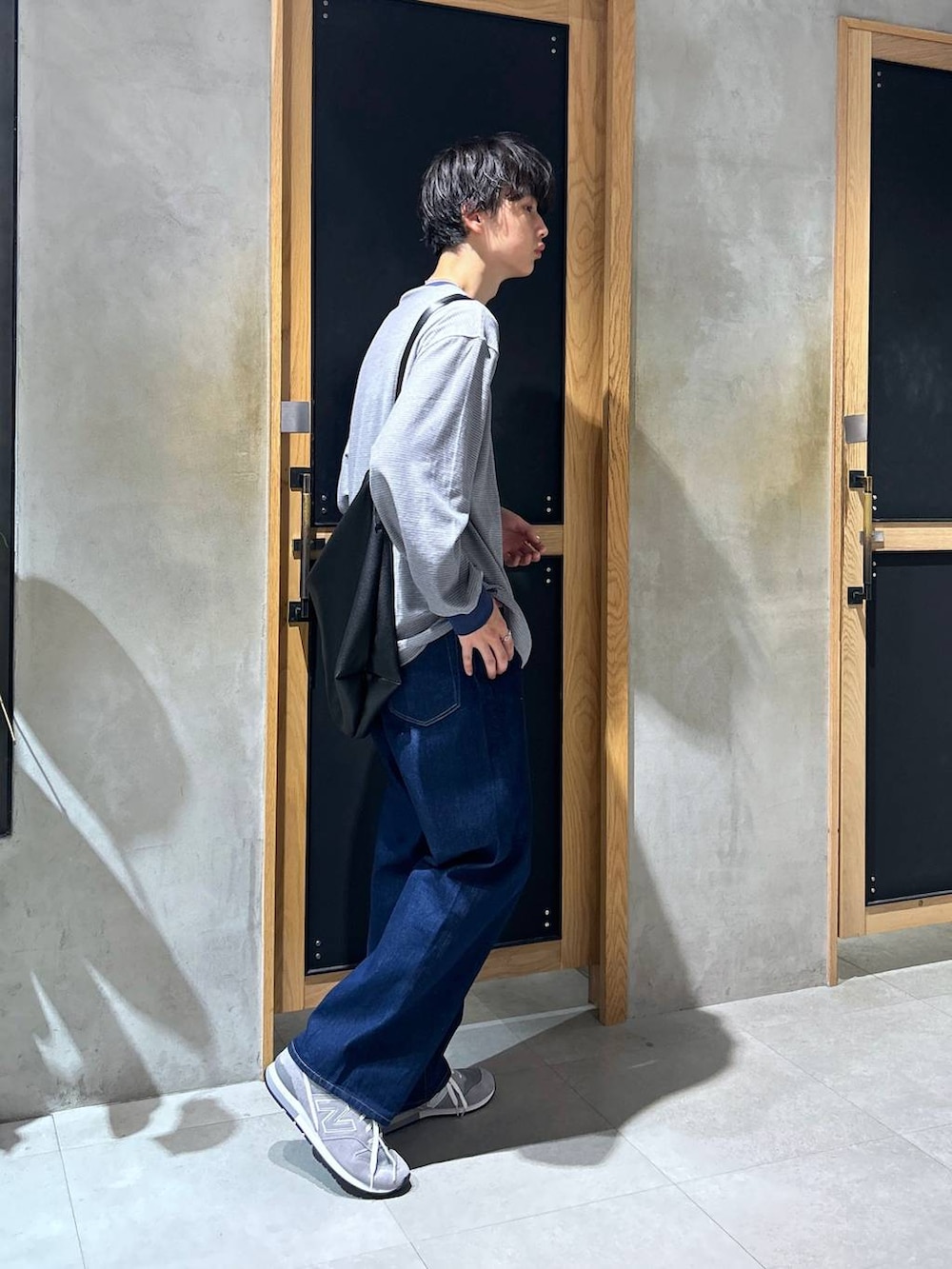 グレー系のスニーカー、ブルー系のデニムパンツ、ブラック系のショルダーバッグを着用したメンズの秋コーディネートの3枚目の写真