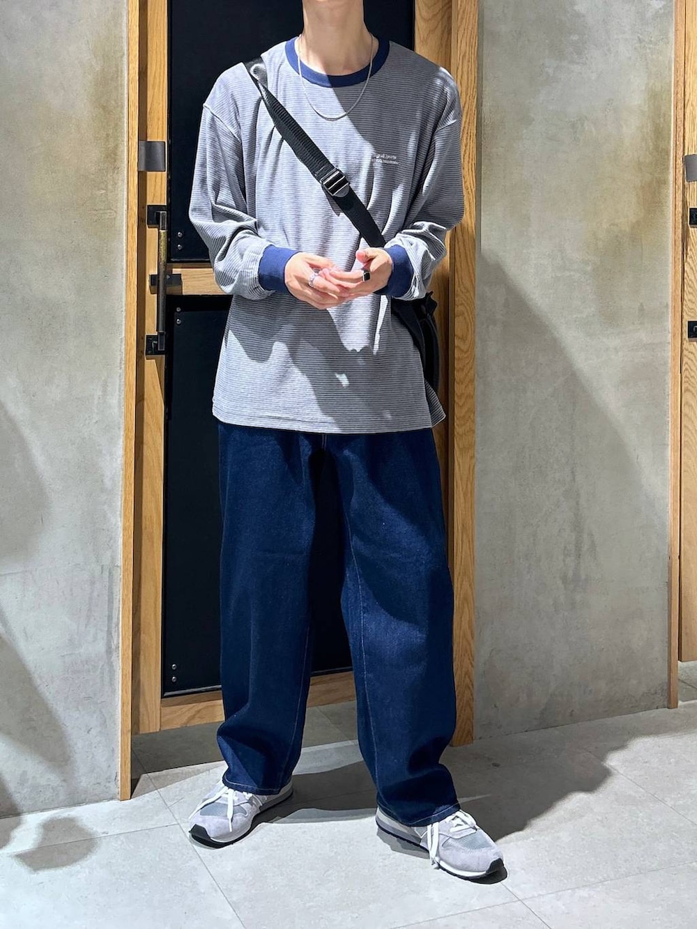 グレー系のスニーカー、ブルー系のデニムパンツ、ブラック系のショルダーバッグを着用したメンズの秋コーディネートの2枚目の写真