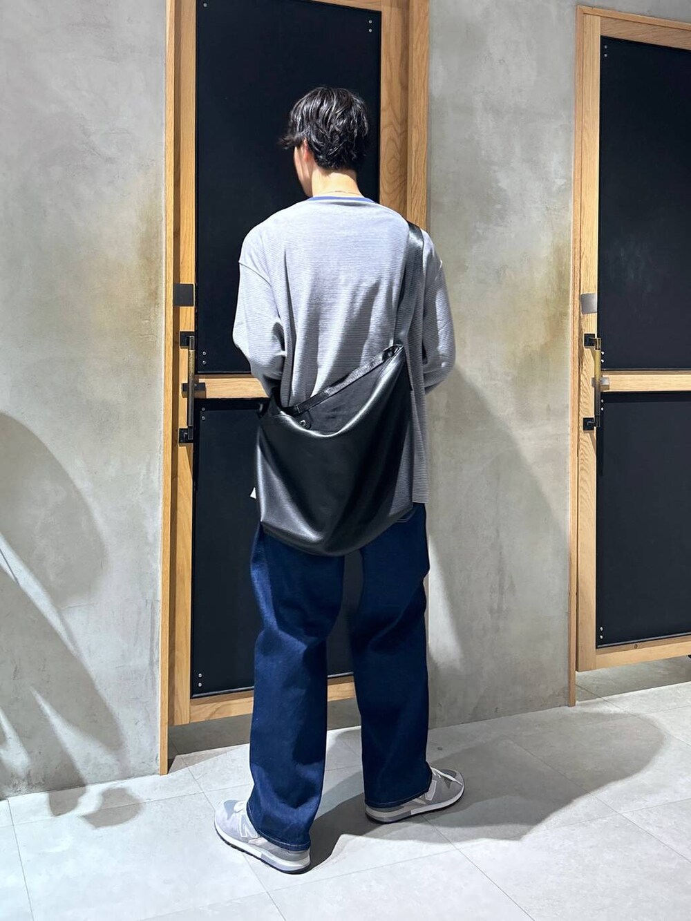 グレー系のスニーカー、ブルー系のデニムパンツ、ブラック系のショルダーバッグを着用したメンズの秋コーディネートの5枚目の写真