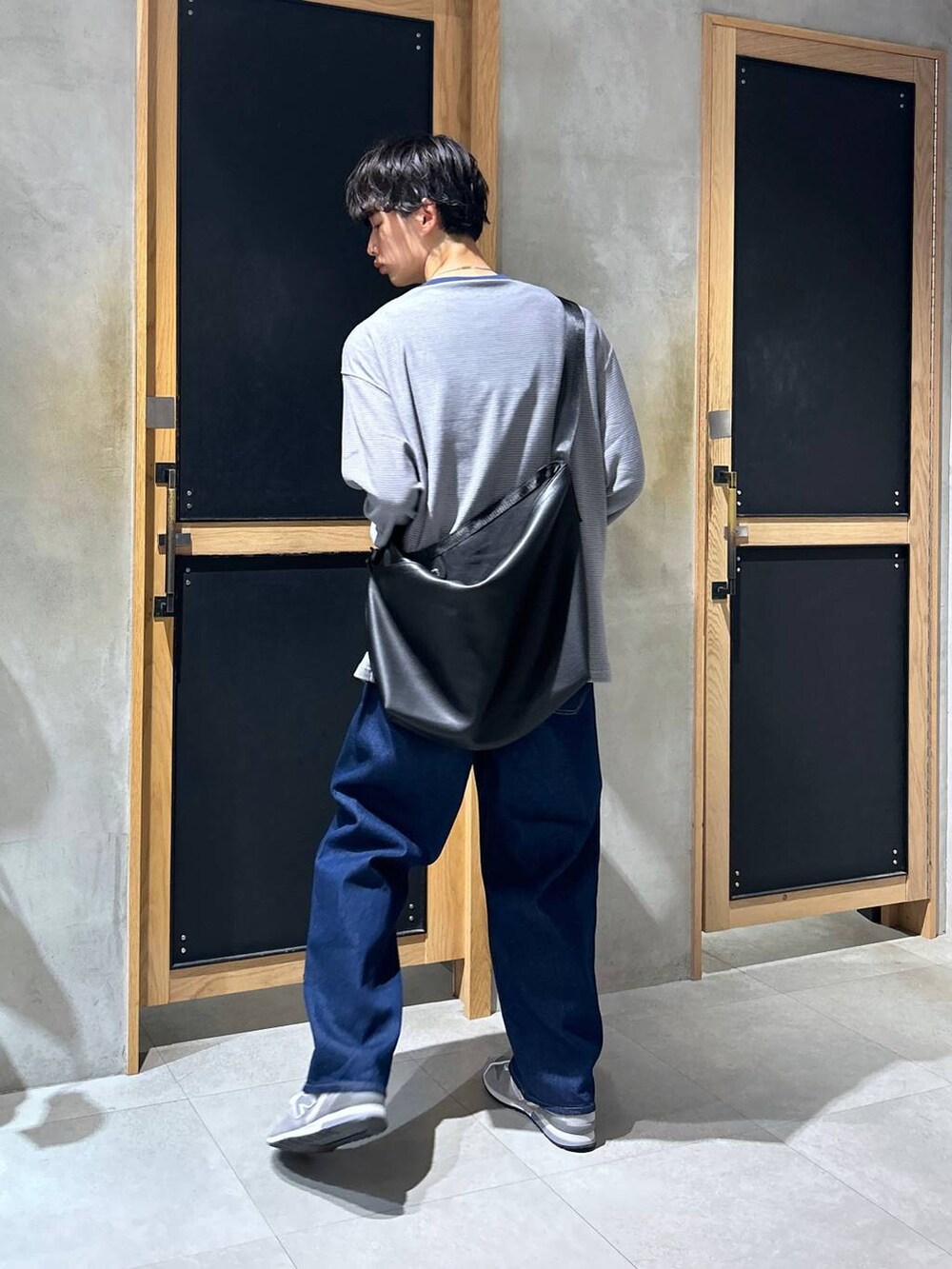 グレー系のスニーカー、ブルー系のデニムパンツ、ブラック系のショルダーバッグを着用したメンズの秋コーディネートの4枚目の写真