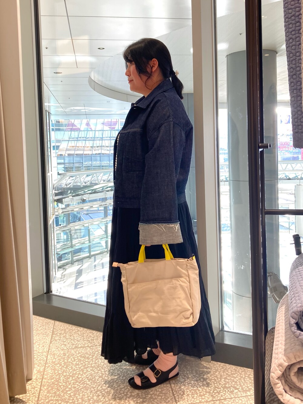 ブルー系のデニムジャケット、ベージュ系のトートバッグ、ブラック系のサンダルを着用したレディースの春コーディネートの2枚目の写真