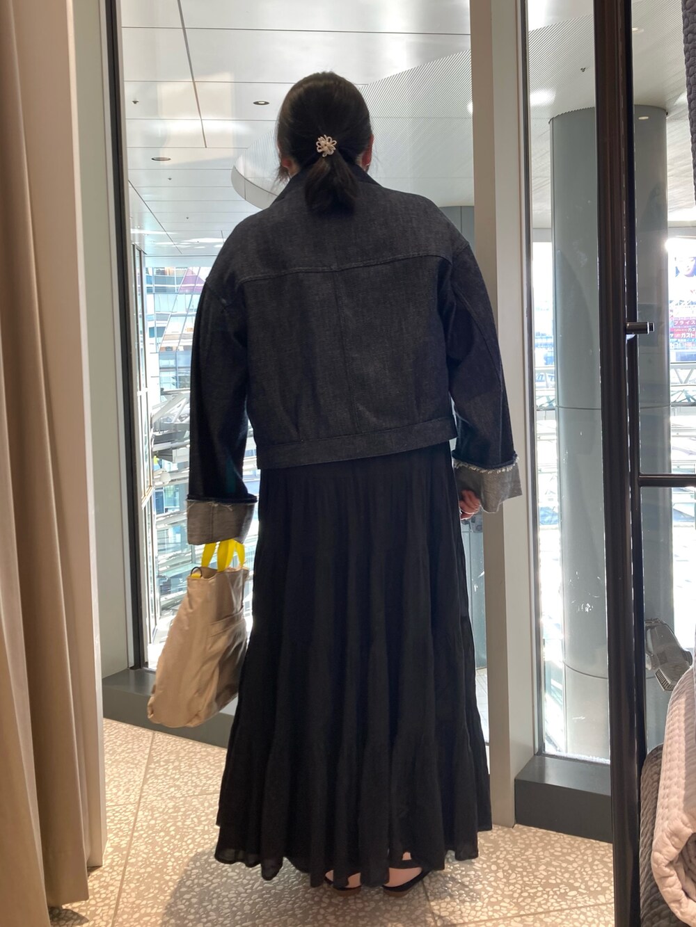 ブルー系のデニムジャケット、ベージュ系のトートバッグ、ブラック系のサンダルを着用したレディースの春コーディネートの3枚目の写真