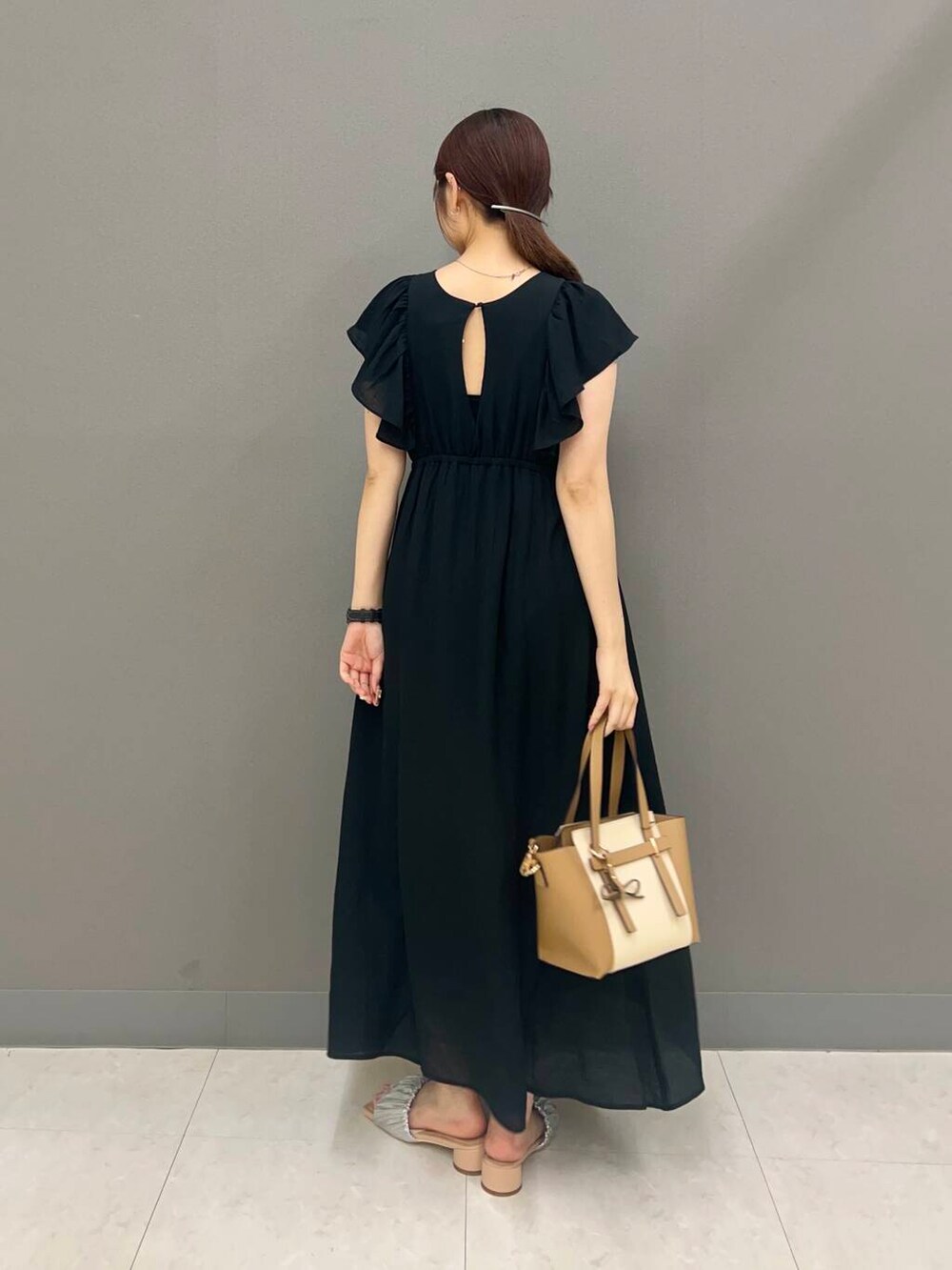 ベージュ系のトートバッグ、シルバー系のサンダル、ブラック系のワンピースを着用したレディースの夏コーディネートの2枚目の写真