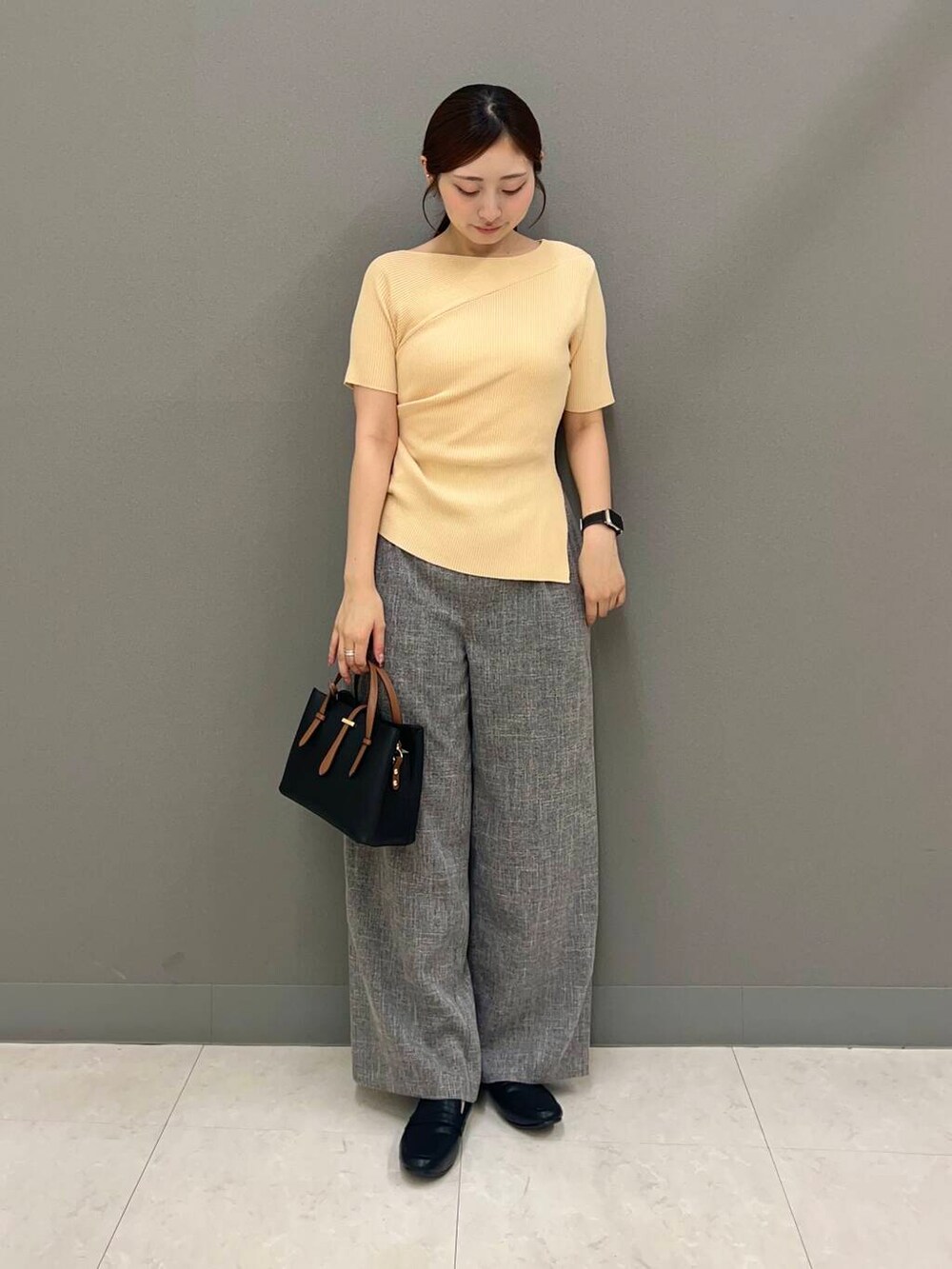 ブラック系のハンドバッグ、ブラック系のローファー、ベージュ系のニット/セーターを着用したレディースの夏コーディネートの2枚目の写真