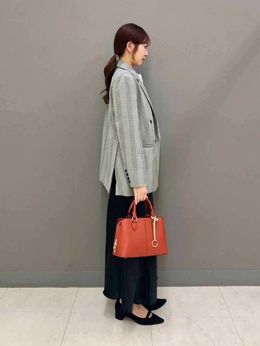 オレンジ系のハンドバッグ、ブラック系のパンプス、ブラック系のスカートを着用したレディースの春コーディネートの3枚目の写真